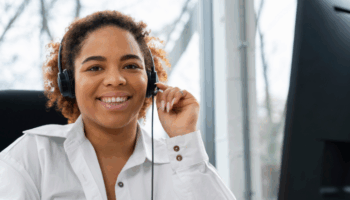 Femme agent en centre de contacts, casque sur les oreilles, souriante devant son ordinateur pendant un pic d’activité