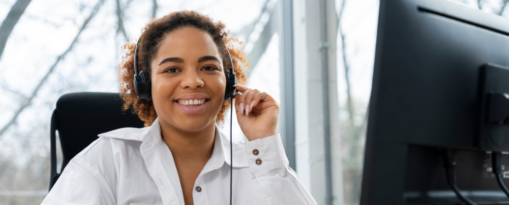 Femme agent en centre de contacts, casque sur les oreilles, souriante devant son ordinateur pendant un pic d’activité